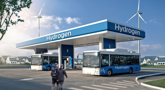 Two people walking towards a hydrogen station with two parked busses.
