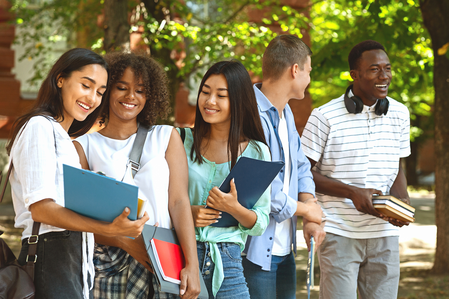 Group of international students resting in campus outdoors during break in classes, chatting and smiling