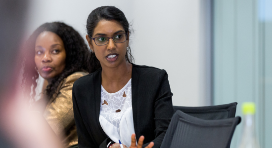woman at a desk explaining something while another woman watches over her shoulder