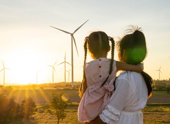 Woman with Daughter looking on Field with Wind Turbines