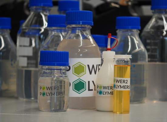 Chemistry glass bottles with fluids in them, labled "Power2Polymers"; close-up