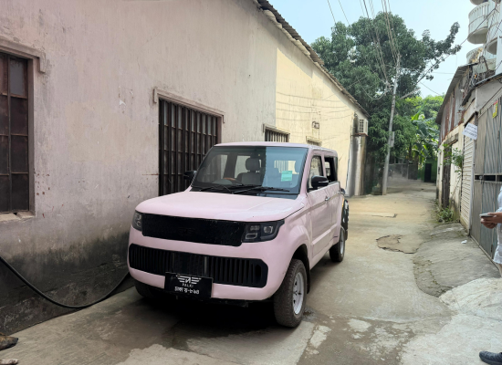 A light-pink car in a street in Bangladesh, from the front